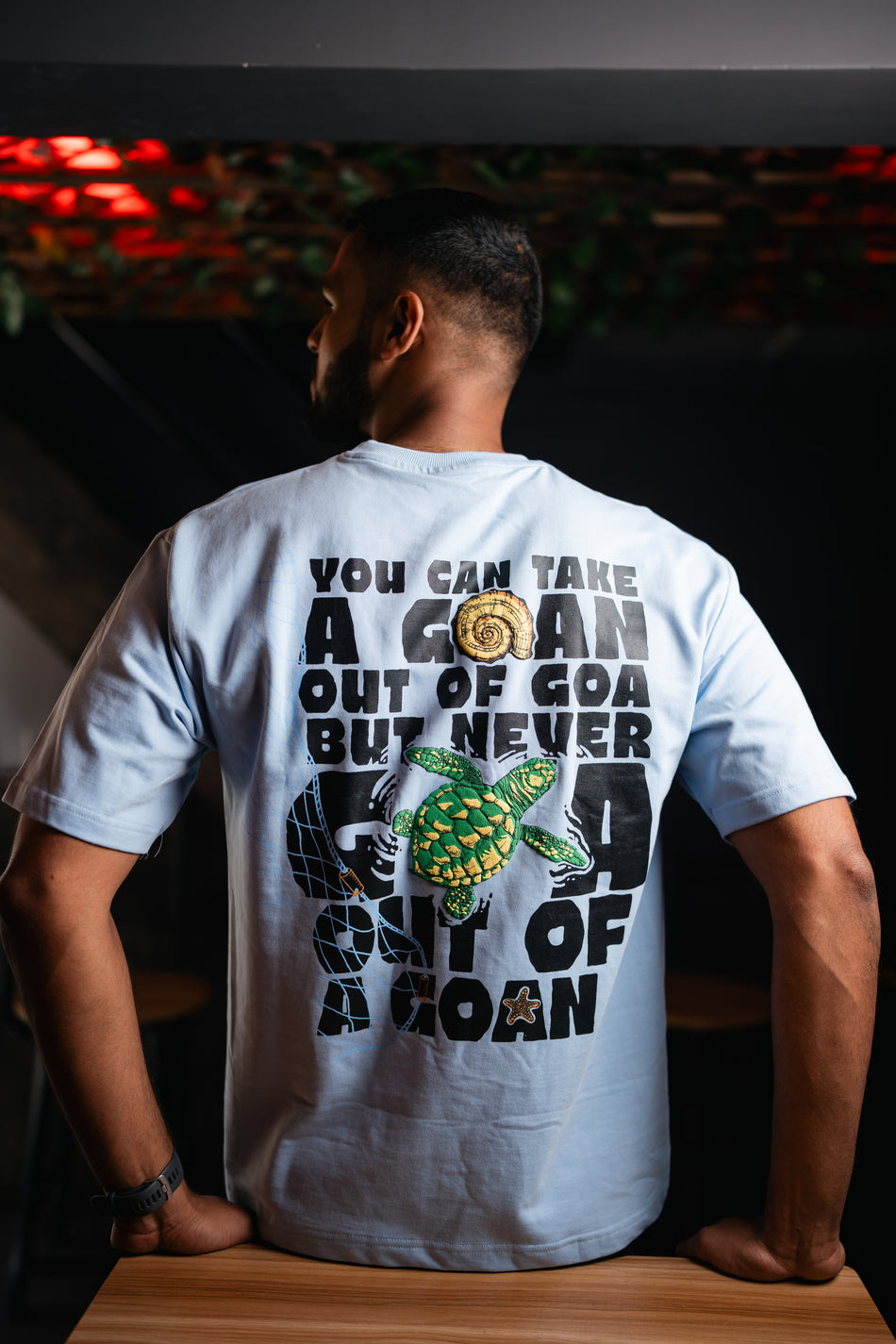 Person wearing a t-shirt with text and graphics on the back, standing indoors.